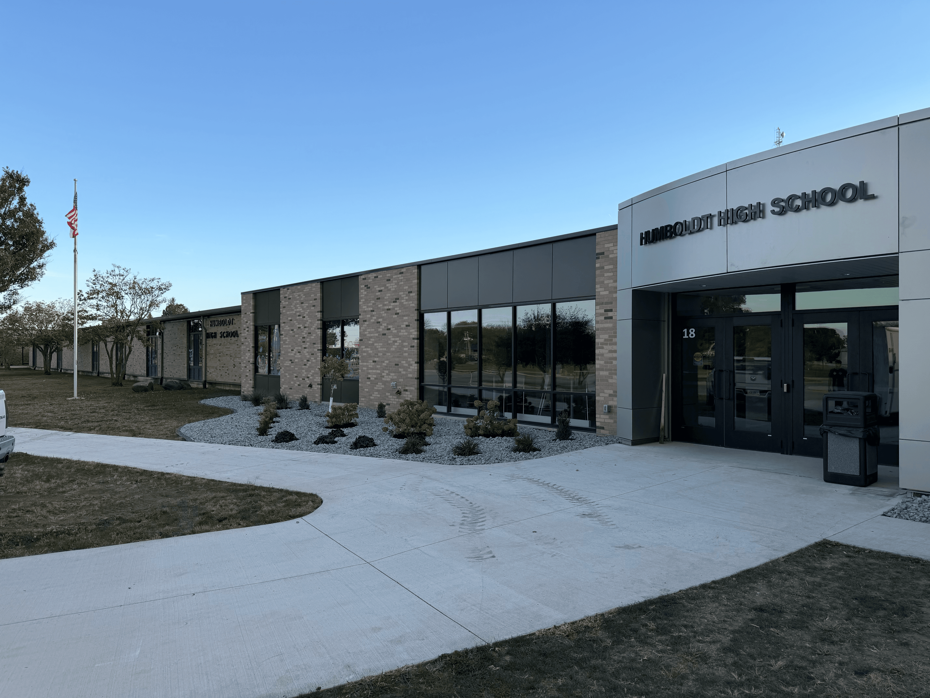 Modern brick and glass facade of Humboldt High School with a flagpole and concrete walkway.