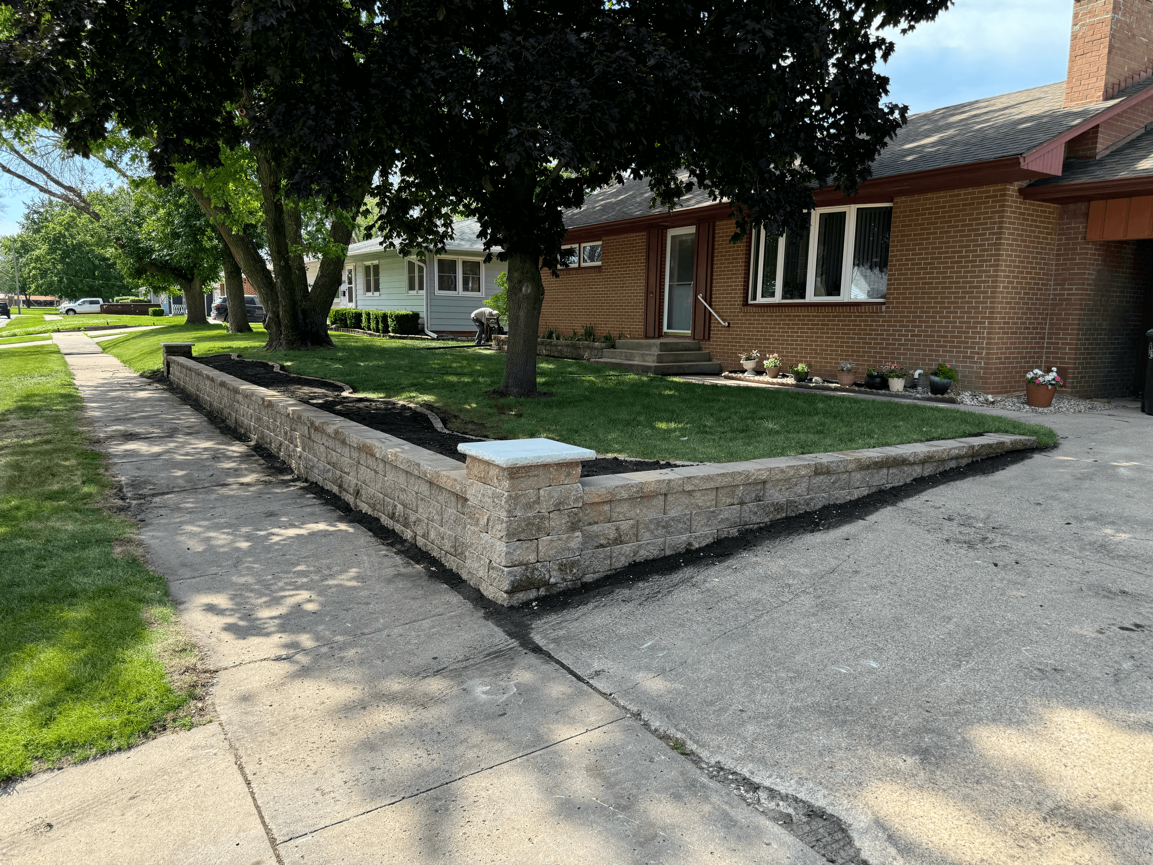 Stone retaining wall bordering the front lawn and driveway of a brick house.